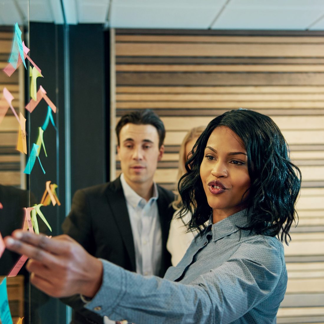 Black business woman in front of mixed business team. Having a standing meeting brainstorming ideas using posters on wall